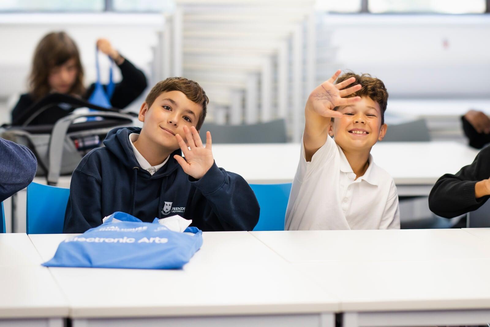 Two children wave smiling at the camera at the Digital Schoolhouse Festival of Play